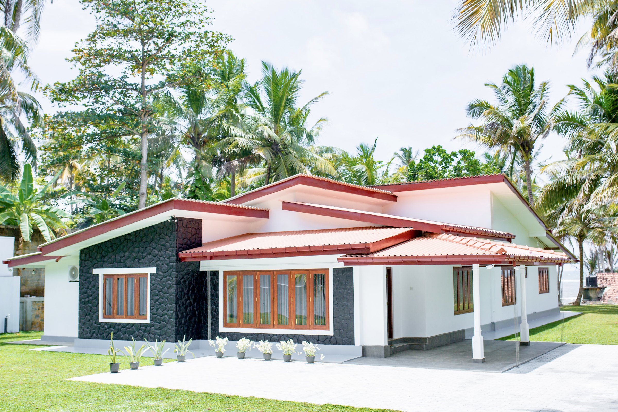 The front of Oceania Villa with its stone-clad wall, palm garden and red-tiled roof